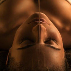 Woman laying on a table with a stream of oil on her forehead.