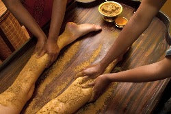 each Leg of a body massaged by two people using an orange powder